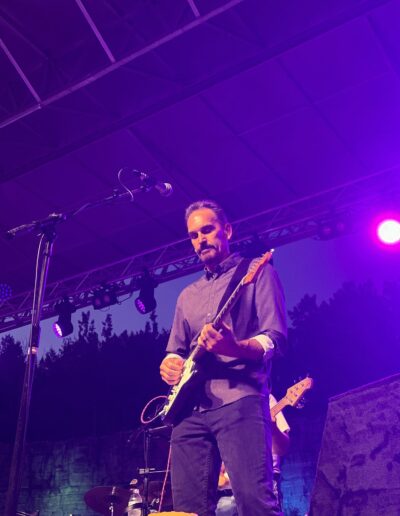 A guitarist performing under purple stage lights at night